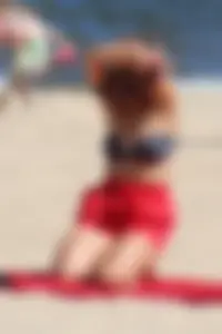 Hottie undressing from her red shorts to her bikini to layout on the beach