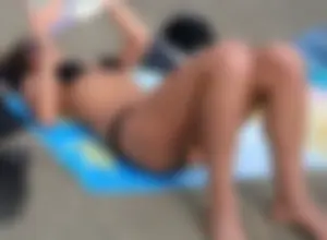 Lady in black bikini showing some pubes while laying out
