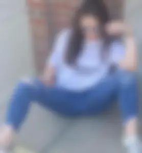 Girl wearing blue ripped jeans sitting on the ground with spread legs on the street