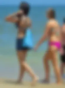 Hot beach brunette in shorts and bikini top with her friend in bikini