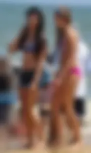 Hot beach brunette in shorts and bikini top with her friend in bikini