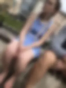 Candid girl wearing shorts sitting on the street bench, took off her shoes