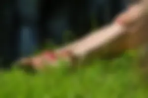 Closeup creepshot of a girl's legs and feet in sandals: sitting on the grass in a park