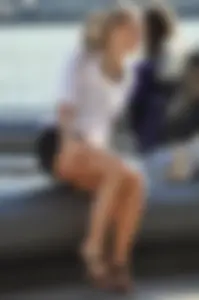 Fair-Haired Girl in Shorts And Platform Sandals Sitting on a Stone Bench on the City Street Creepshot