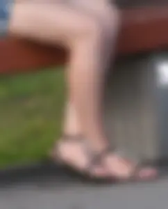 Hot bare legs and feet in sandals of a candid girl chilling on a street bench closeup creepshot