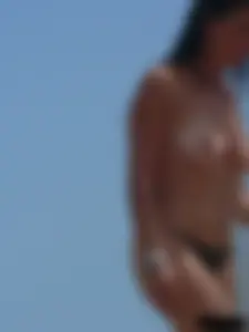 Brunette lady topless and in a black thong on the beach