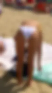 Candid blonde beach girl in white bikini bottom bending over