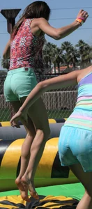 Brunette skinny teen in green shorts playing in a bounce house