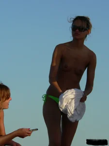 Topless girl on the beach with small boobs wearing a green thong bikini