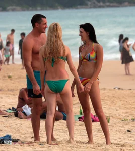 Sexy brunette in thong bikini and blonde friend in green bikini at the beach