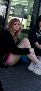Awesome teen girl with pink dyed hair in hosrts sitting on the ground at the bus stop