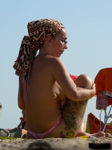 Topless tattooed lady at the beach with a nice ass in pink thong bikini