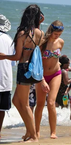 Hot beach brunette in shorts and bikini top with her friend in bikini