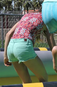 Brunette skinny teen in green shorts playing in a bounce house