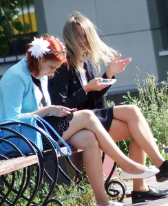 Girls in Skirts and Fishnet Stockings Sitting on the Bench in City Park