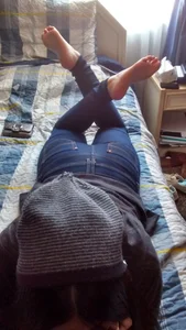 Barefoot Girl in Jeans and a Hoodie Lying in Bed on Her Tummy Dangling Her Feet in the Air