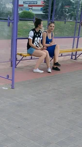Two candid teen girls sitting on bench at bus stop
