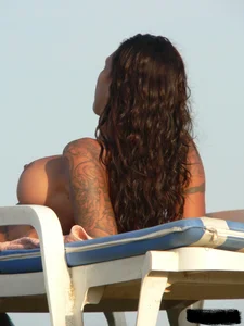 Topless tattooed lady on the beach with fake big tits