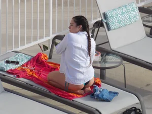 Sexy ass brunette sunbathing by the pool in thong bikini