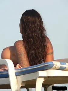 Topless tattooed lady on the beach with fake big tits