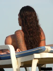 Topless tattooed lady on the beach with fake big tits