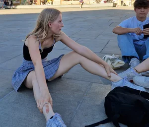 Young Skinny Girl in a Skirt Sitting With Legs Wide Apart on the Pavement, Flashing Her Panties