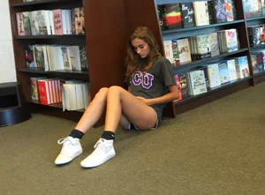 Cute skinny teen in shorts sitting on the floor at the book store