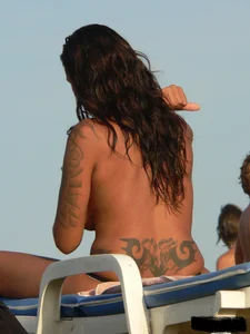 Topless tattooed lady on the beach with fake big tits