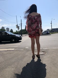 Hot street candid girl wearing a short dress and sandals standing on the crosswalk, wind is playing with her hair