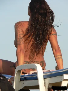 Topless tattooed lady on the beach with fake big tits
