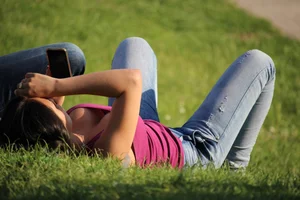 Skinny Candid Girl in Jeans Lying on the Grass in the Park, Downblouse Photo
