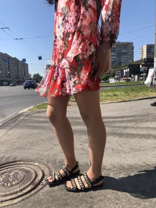 Hot street candid girl wearing a short dress and sandals standing on the crosswalk, wind is playing with her hair