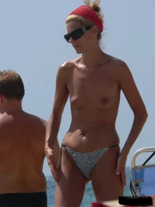 Topless skinny blonde lady in a g-string bikini at the beach