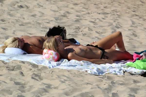 Topless mom and daughter on the beach getting some sun