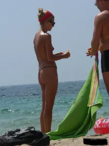 Topless skinny blonde lady in a g-string bikini at the beach