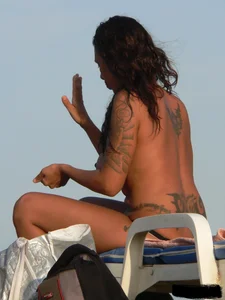 Topless tattooed lady on the beach with fake big tits