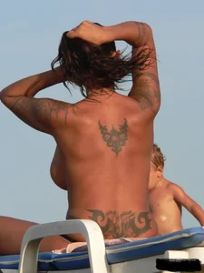 Topless tattooed lady on the beach with fake big tits