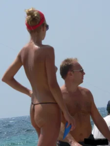 Topless skinny blonde lady in a g-string bikini at the beach