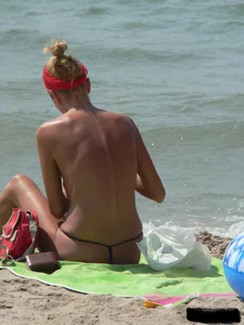 Topless skinny blonde lady in a g-string bikini at the beach