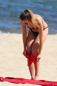 Hottie undressing from her red shorts to her bikini to layout on the beach