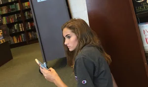 Cute skinny teen in shorts sitting on the floor at the book store