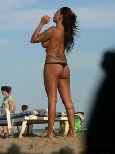 Topless tattooed lady on the beach with fake big tits
