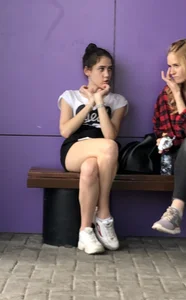 Girl in Shorts abs Sneakers Sitting With Crossed Legs on the Street Bench Creepshots