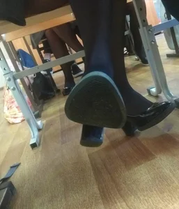 College Girl's Under Desk Feet Closeup in Black Pantyhose And High-Heeled Shoes