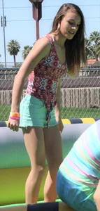 Brunette skinny teen in green shorts playing in a bounce house
