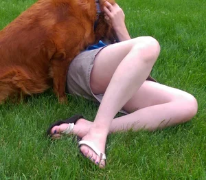 Candid girl in a skirt and sandals lying on the grass in a park, hot pale legs