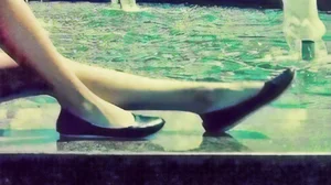 Slim Legs And Feet in Flats of a Young Girl Sitting on the Border of a Fountain