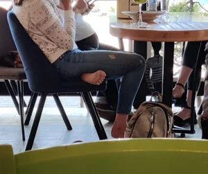 Skinny barefoot teen wearing torn tight blue jeans in a cafe