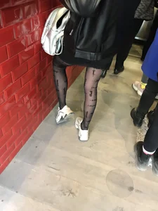 Sexy skinny legs in black pantyhose with dots and sneakers closeup creepshot in a cafe