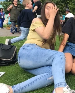 Teen in blue jeans sitting on the grass in the park creepshot